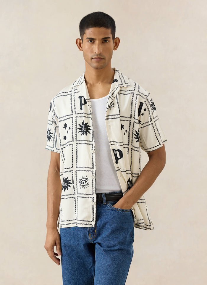 The cream Percival Lunar Panel Cuban Shirt in viscose, featuring black celestial prints, worn by a model in blue jeans.