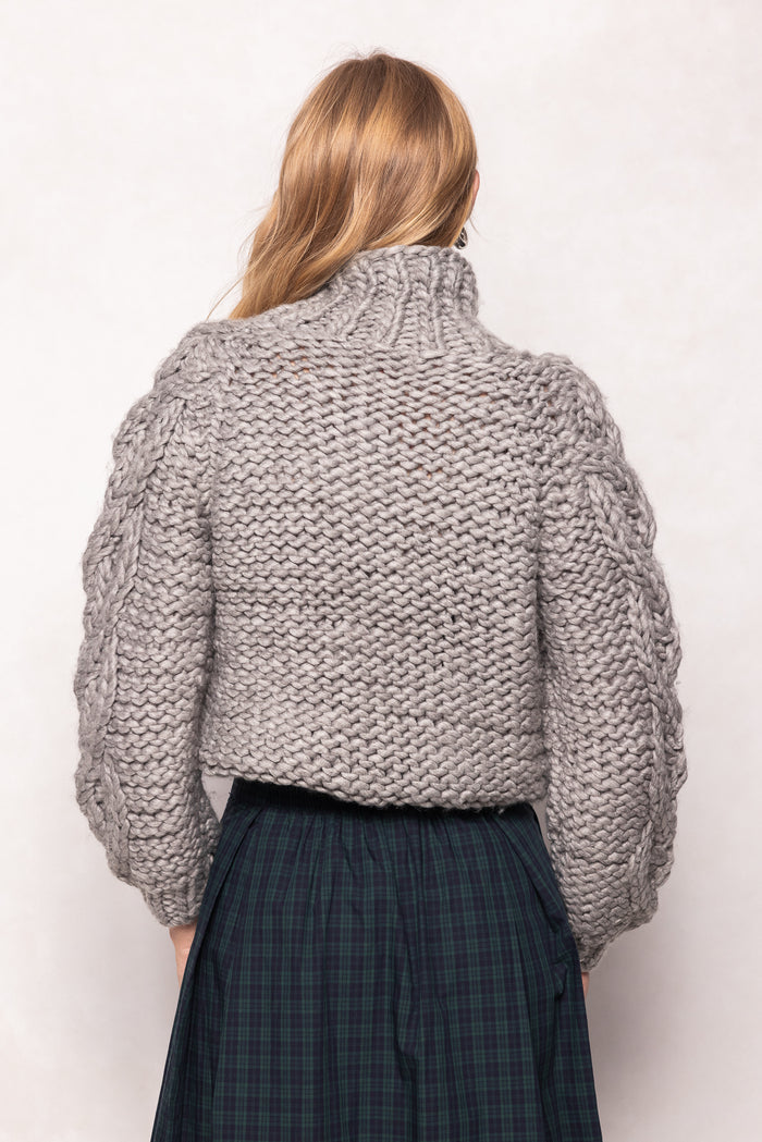 Person wearing a chunky knit gray sweater on a white background