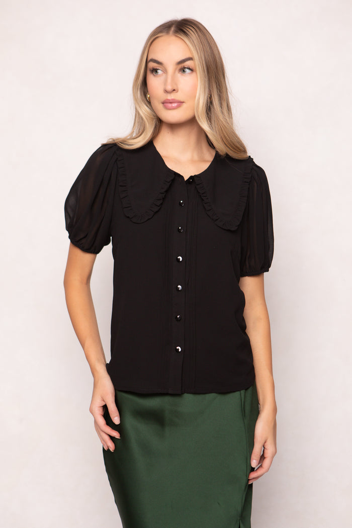 Woman wearing a black blouse with a large collar against a white background