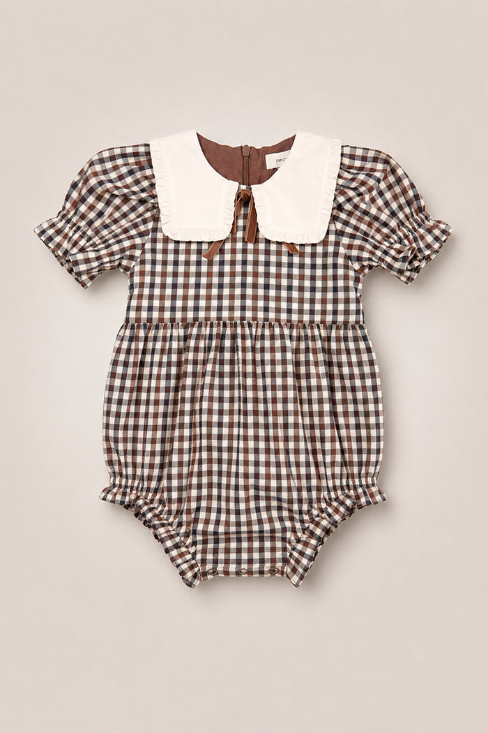 The Baby Emery Romper in Chestnut Gingham by Ivy City Co features a charming brown and white gingham cotton design with short puffed sleeves, ruffled leg openings, and a large white collar. This vintage-inspired romper combines classic style with comfort for your little one and includes a back button closure.