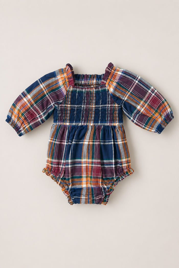 The Baby Madeline Romper in Midnight Plaid by Ivy City Co showcases long puff sleeves and a multicolored plaid pattern in shades of blue, orange, red, and yellow. Delicate ruffle details accent the shoulders and leg openings, adding extra charm to this adorable outfit.
