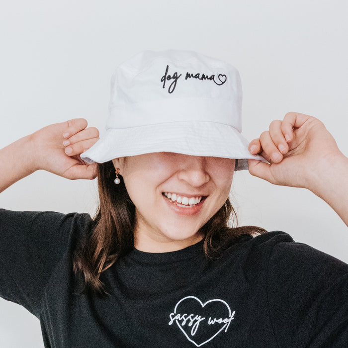 A woman poses with hands on her Bucket Hat - Dog Mama by Sassy Woof, paired with a black Sassy Woof tee featuring a heart, against a plain white background.