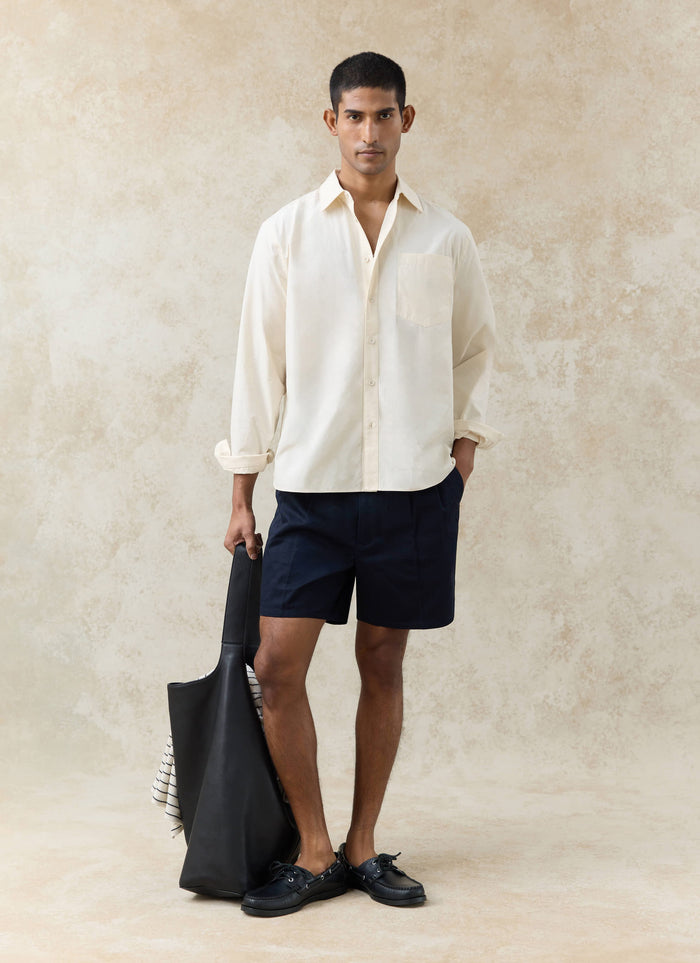 Percival Dali Relaxed Poplin Shirt in cream cotton, styled with navy shorts and a black tote bag on a model.