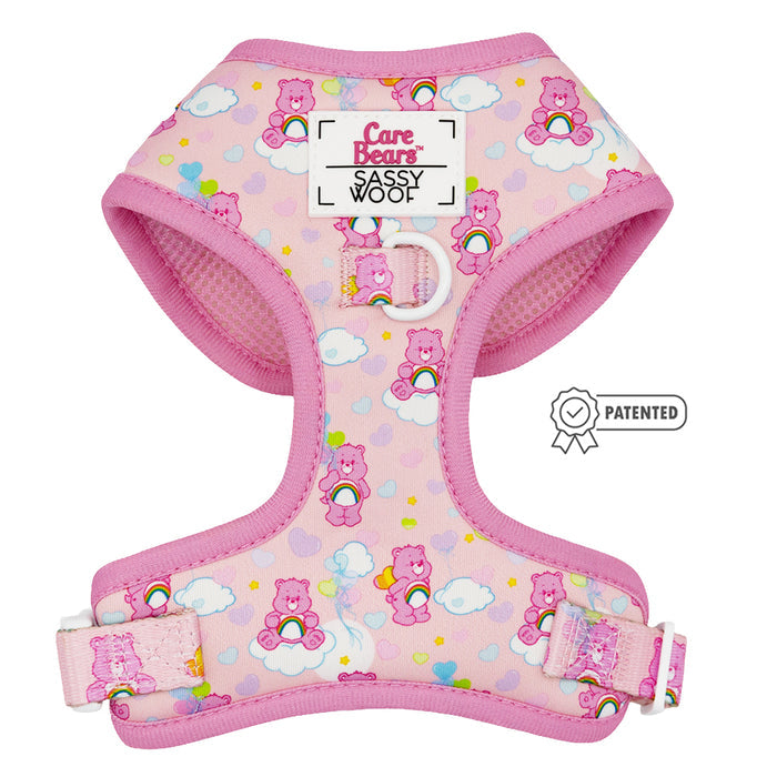 The Sassy Woof Dog Adjustable Harness - Care Bears™ Cheer Bear features a pink design with clouds and hearts, "Care Bears Sassy Woof" on the front, a metal D-ring, patented badge, and supports the Puppy Growth Pawtection Plan.