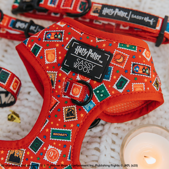 The Sassy Woof Dog Adjustable Harness - Harry Potter™ Stamps features magical stamp designs and logos, shown on a white knitted surface next to a lit candle.