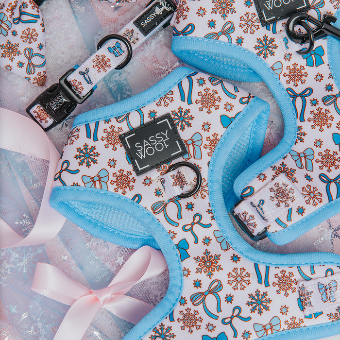 The Sassy Woof Dog Adjustable Harness - Let it Bow features blue trim, festive gingerbread cookie patterns, and is showcased on sheer pink fabric with ribbons—perfect for adding holiday charm to your dog's style.