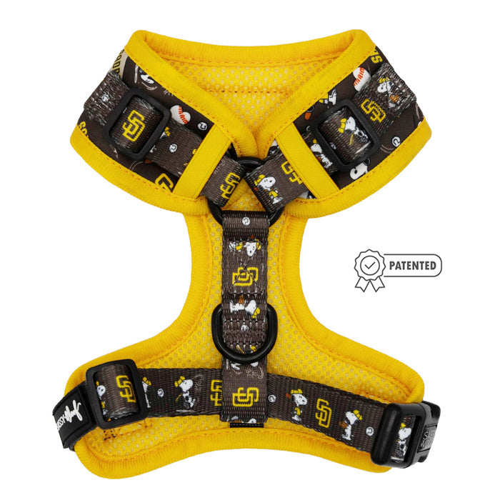 The Sassy Woof Dog Adjustable Harness - MLB™ x Peanuts™ San Diego Padres™ features yellow trim, black straps, Snoopy baseball graphics, and team logos. It offers puppy growth protection and displays a Patented badge to the right.