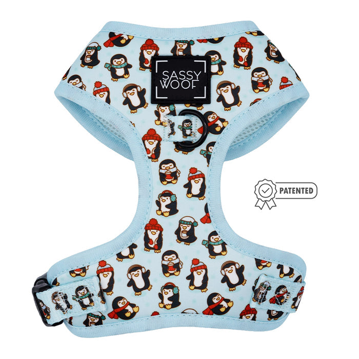 The Dog Adjustable Harness - Winter Waddleland by Sassy Woof features light blue fabric with penguins in hats and scarves, a black Sassy Woof logo patch on the front, and a patented badge—perfect for winter dog accessories.