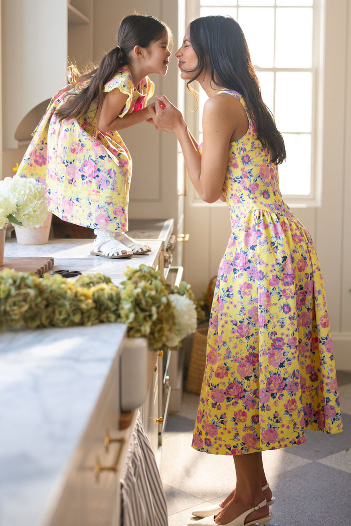 A woman and young girl smile and touch noses in a bright kitchen, wearing matching Ivy City Co Edith Dresses in As You Dream Floral. The girl stands on the counter as the woman stands beside her, holding her hands.