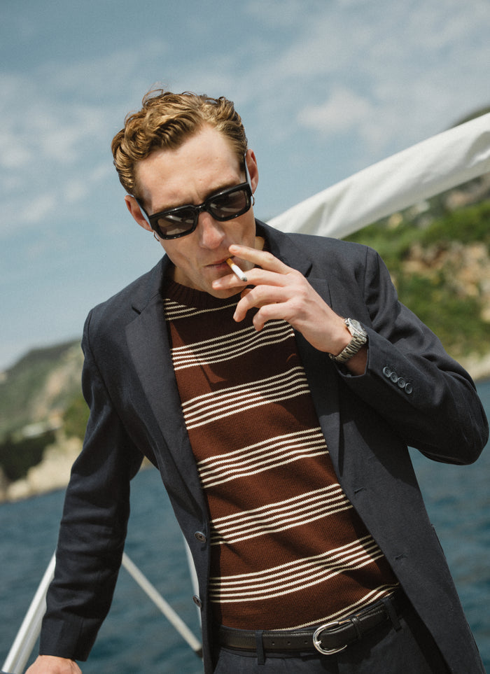 The Percival Fiction Knitted T-Shirt in espresso brown with ecru stripes, layered under a blazer on a boat.