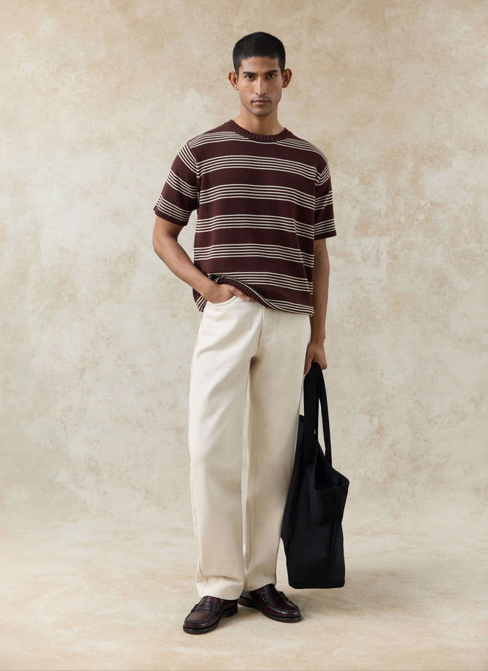 The Percival Fiction Striped Knitted T Shirt in espresso brown, styled with cream trousers and a black tote bag.