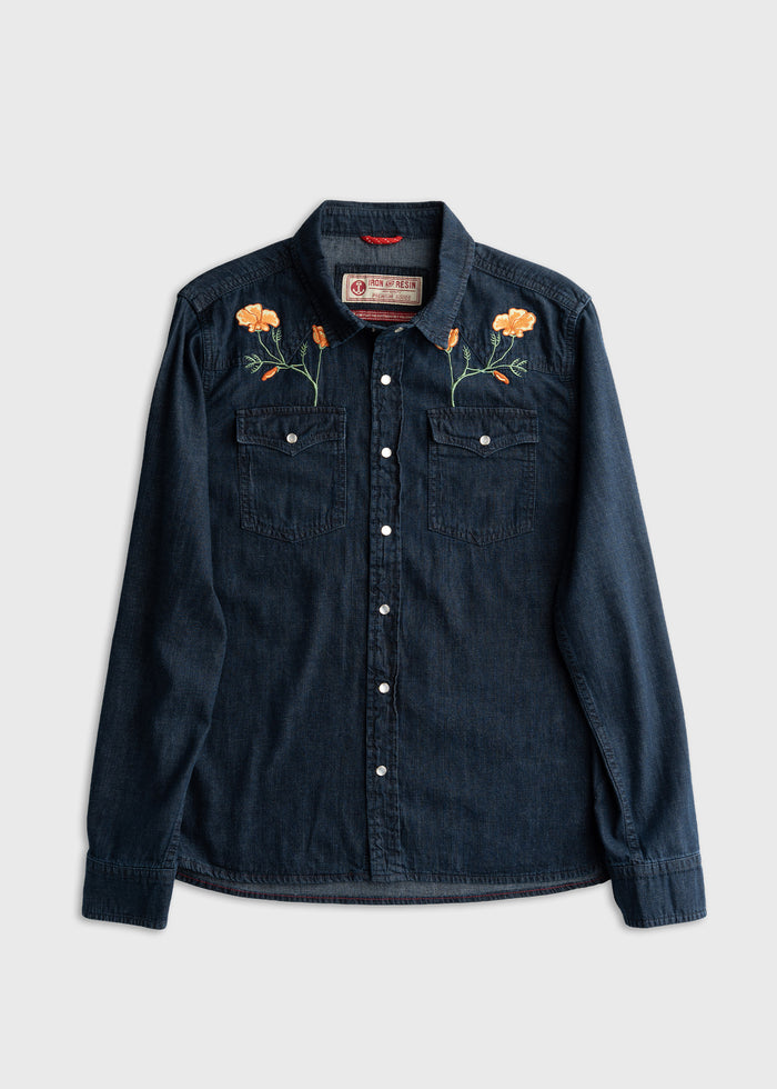 Dark denim shirt with orange floral embroidery on shoulders, featuring buttoned pockets and a classic collar, laid flat on white.