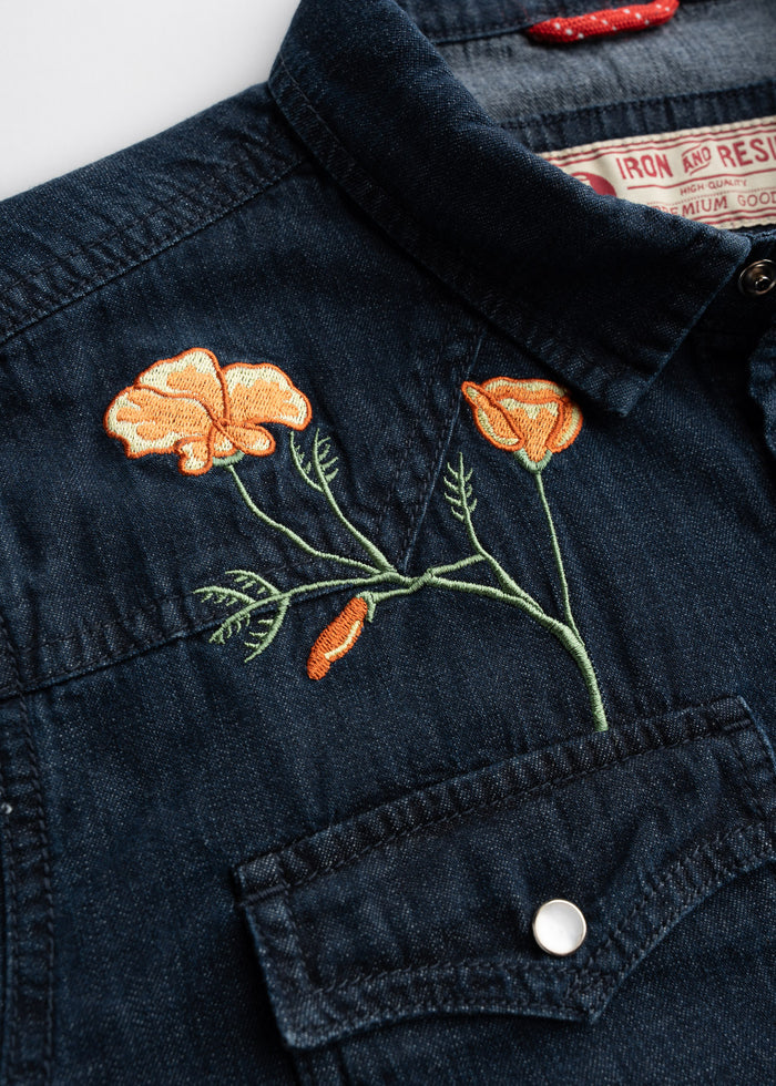 Denim shirt with orange poppy embroidery above pocket, featuring detailed stitching and a visible label inside the collar.