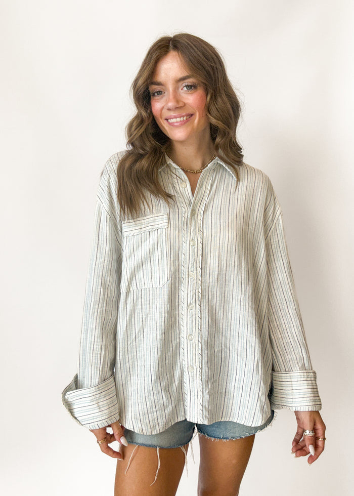 Woman wearing a striped shirt with rolled-up sleeves against a plain background