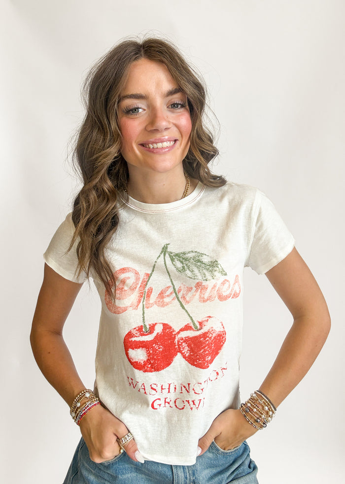 Woman wearing a white t-shirt with red cherries and text on a plain background