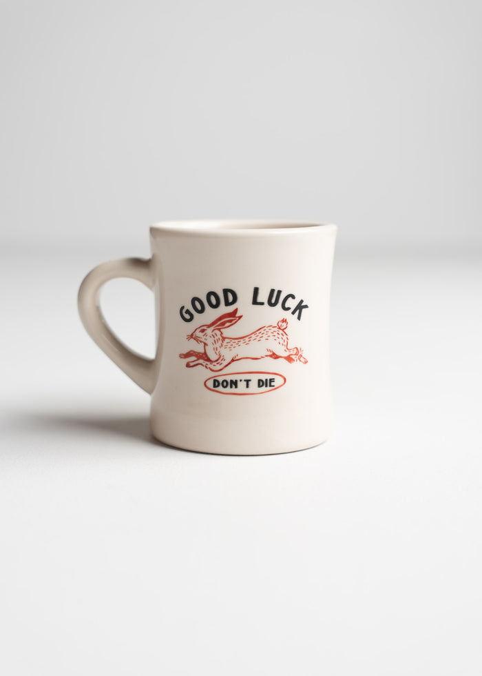 A white mug with a red rabbit design and the words "GOOD LUCK DON'T DIE" in bold letters on a plain background.