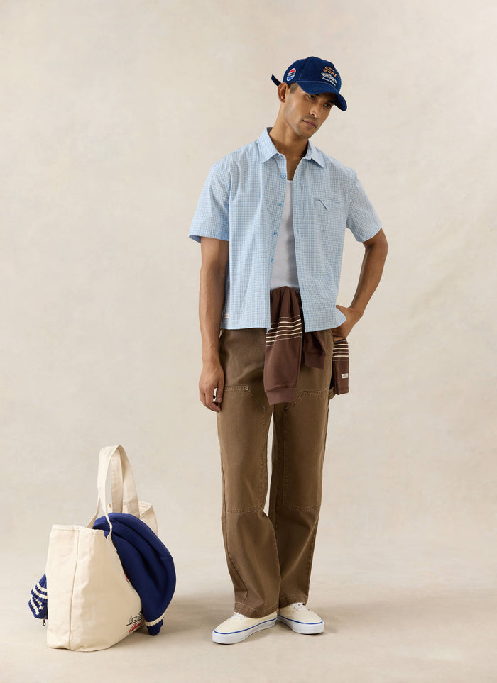 Percival blue check Hinsley boxy cotton shirt, styled with Lucas trousers, an Editor rugby polo, and a blue Spencer cap.