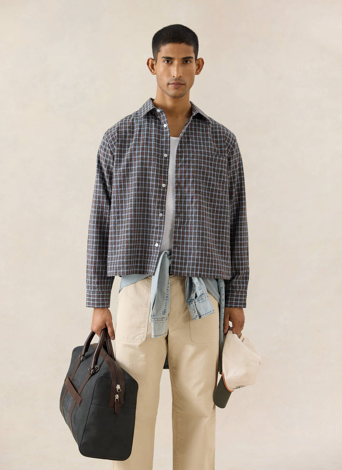 Percival Hinsley brown micro-checked boxy cotton shirt, styled with beige trousers and a black holdall on a model.
