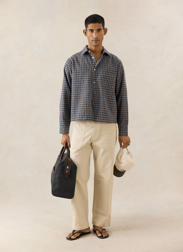 Percival Hinsley brown checked boxy shirt in cotton, worn by a model with beige trousers and a black bag.