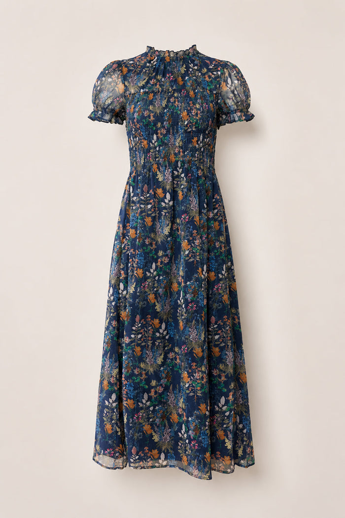 The Leonora Dress in Midnight Autumn Bouquet by Ivy City Co is a navy blue, midi-length dress featuring a floral print, smocked bodice, ruffled high neckline, and sheer puff short sleeves. Displayed against a light background, this versatile piece is also maternity friendly.