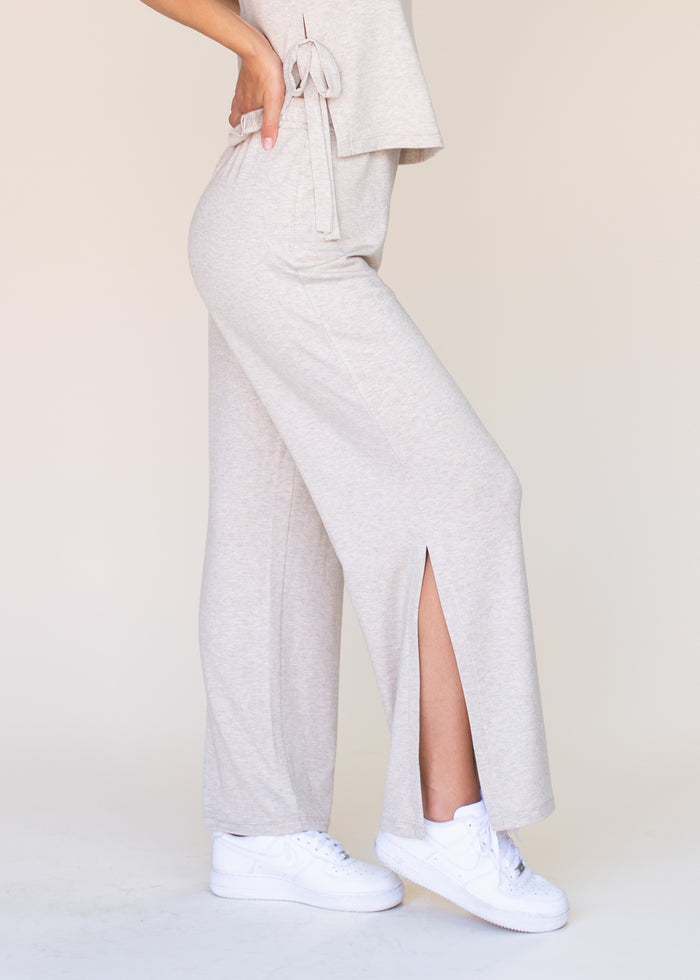 Person wearing light gray sweatpants with a front split and white sneakers on a beige background