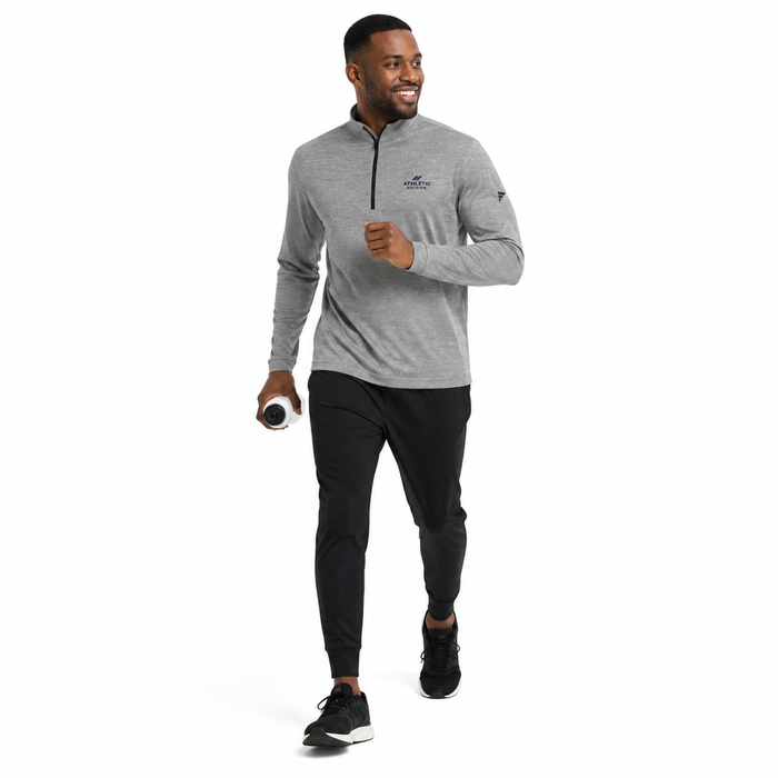 A man jogging while wearing a heather gray long-sleeve quarter-zip athletic pullover with a small logo on the left chest, paired with black joggers and black sneakers, against a solid white background.