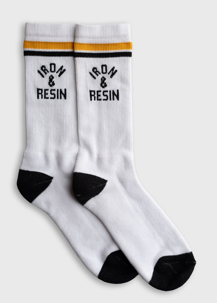 White socks with black toes and heels, featuring "Iron & Resin" text and yellow-black stripes on the cuffs, laid flat on a surface.