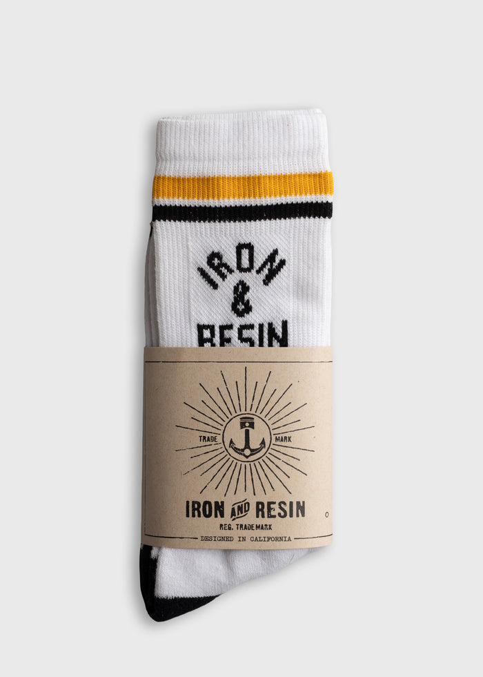 White socks with black and yellow stripes, labeled "Iron & Resin," wrapped in a branded paper band, designed in California.