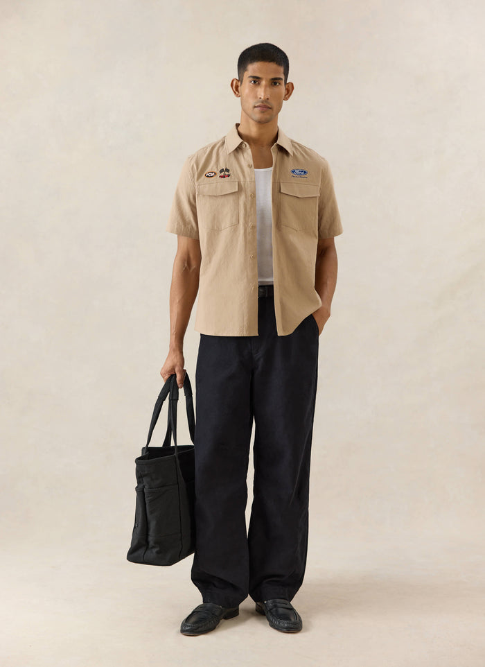 Beige Percival x Ford Miles Garage embroidered cotton-hemp shirt styled with dark trousers and a black tote bag.