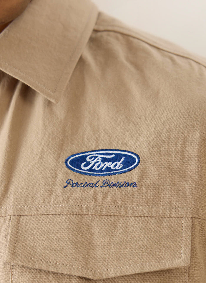 Close-up of the blue Ford logo and Percival Division embroidery on the beige cotton-hemp Miles Garage shirt.
