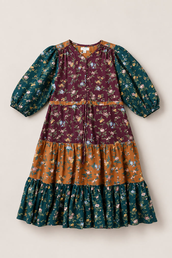 The Mini Harlowe Dress in Elysian Vine by Ivy City Co features long puff sleeves and a tiered midi skirt adorned with floral patterns in burgundy, mustard, and dark teal sections on a neutral background. Made from soft viscose for all-day comfort, this dress offers effortless style.