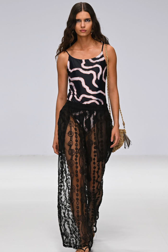 Model wearing Aborigina designed one piece bathers, with sheer black pants on a runway