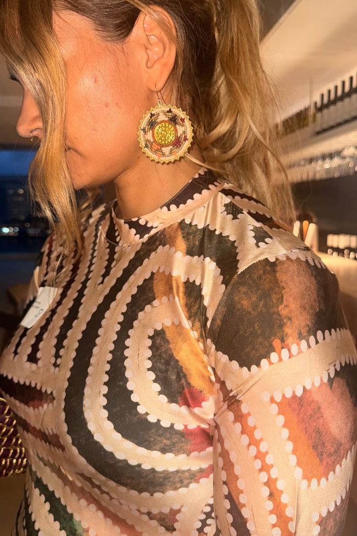 Aboriginal woman wearing a silk Aboriginal dress with beaded earrings in an indoor setting