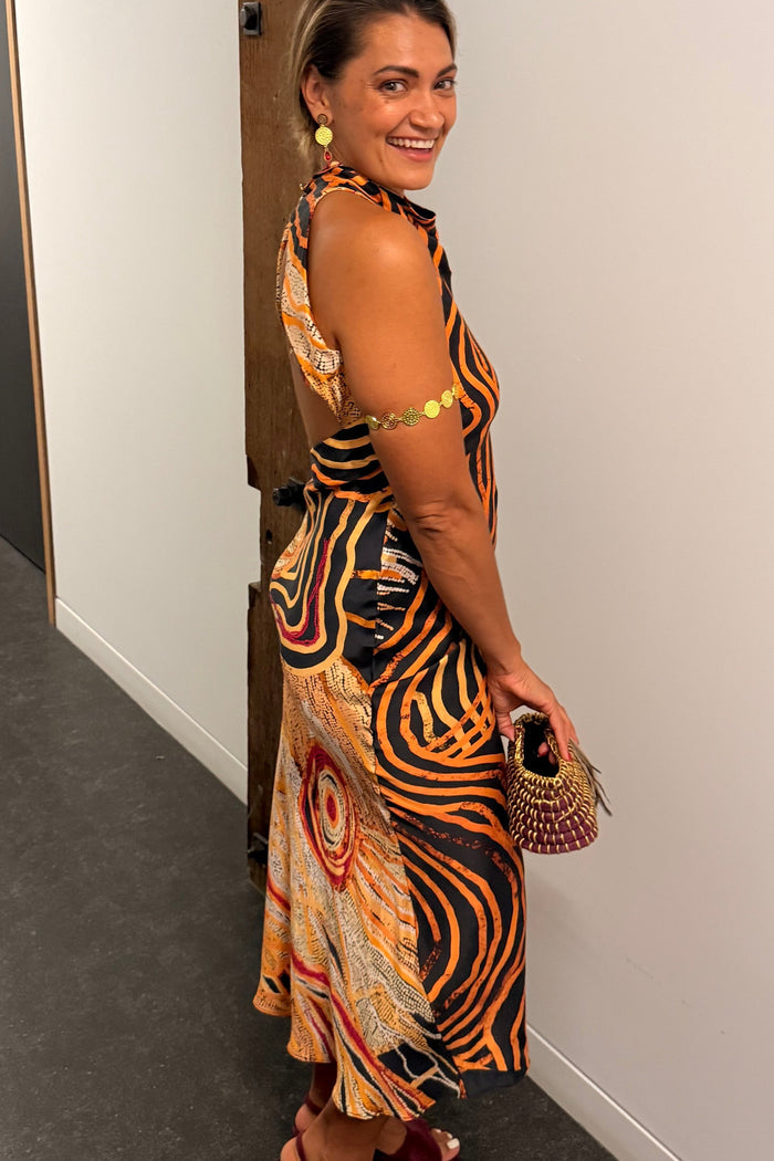 Aboriginal Woman in a First Nations designed dress standing against a white wall.