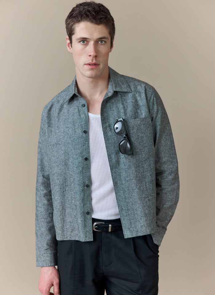 A model wears the grey Textured Boxy Shirt from Percival, styled open over a white vest and paired with black trousers.
