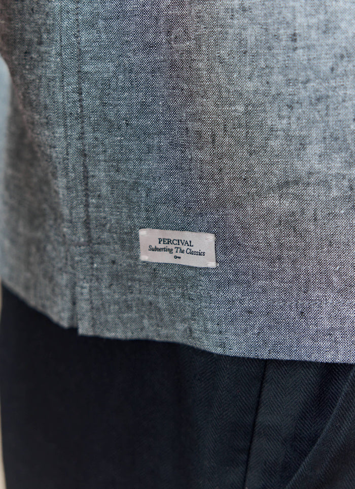 A close-up of the grey Textured Boxy Shirt from Percival, showing the detailed cotton-linen fabric and branded hem label.