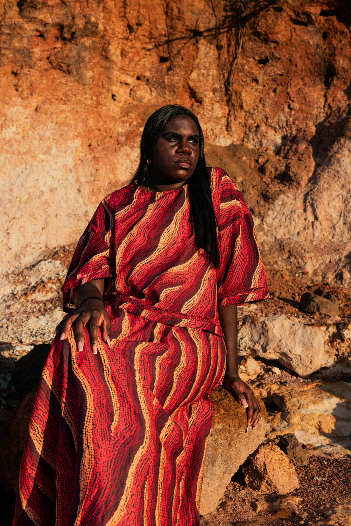 An Aboriginal woman  wearing a tshirt and top with Aboriginal artwork against a rocky background