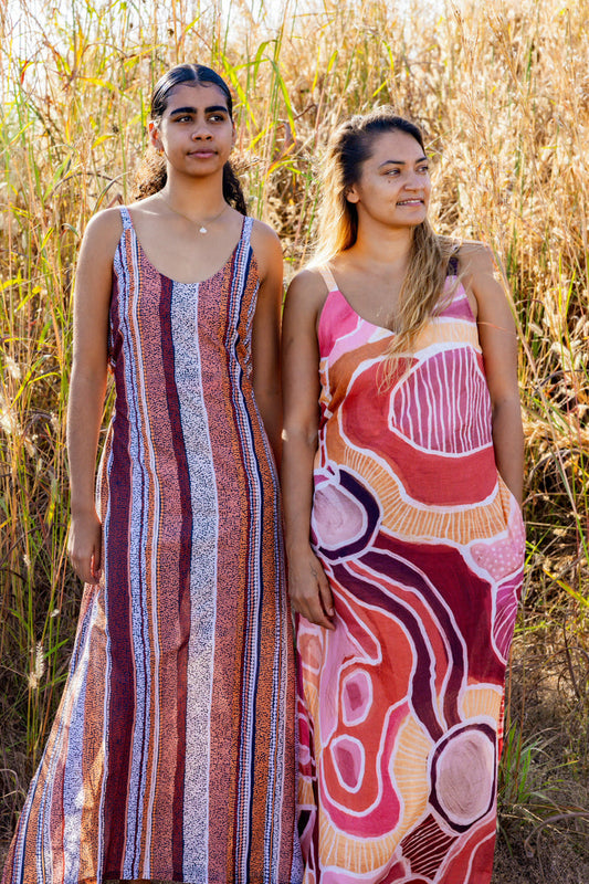 Two women standing in a field wearing Aboriginal patterned dresses.