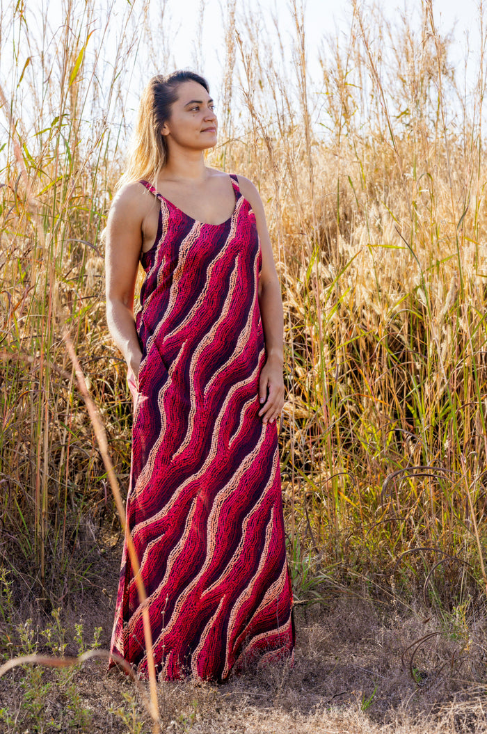 Woman wearing a Aboriginal patterned dress standing in a field with tall grass.