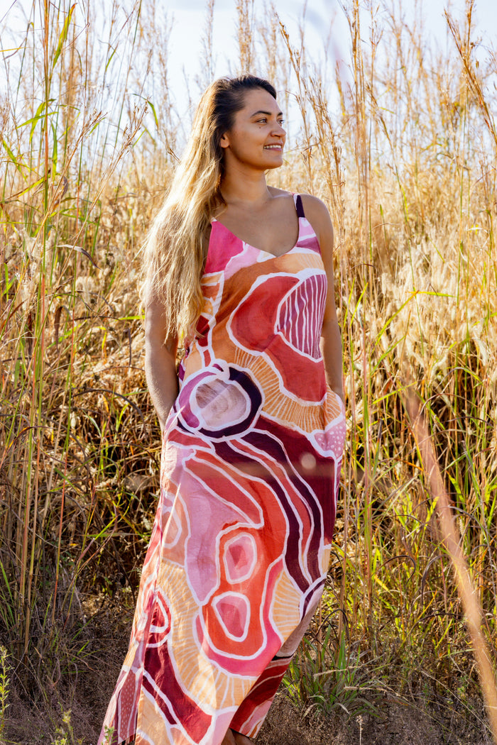 Woman wearing a Aboriginal patterned dress standing in tall grass.