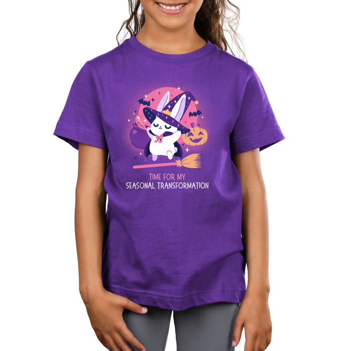 Premium Cotton T-shirt_TeeTurtle purple Time For My Seasonal Transformation apparel featuring a white bunny wearing a sparkling purple witch hat and cloak on top of a flying broom with a cauldron, bats, jack-o'-lantern, and the full red moon in the background.
