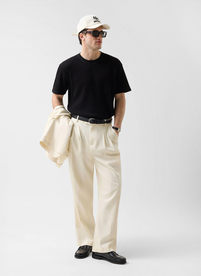 Full-length shot of a model styling the Percival black Waffle Short Sleeve T-Shirt with cream trousers and accessories.
