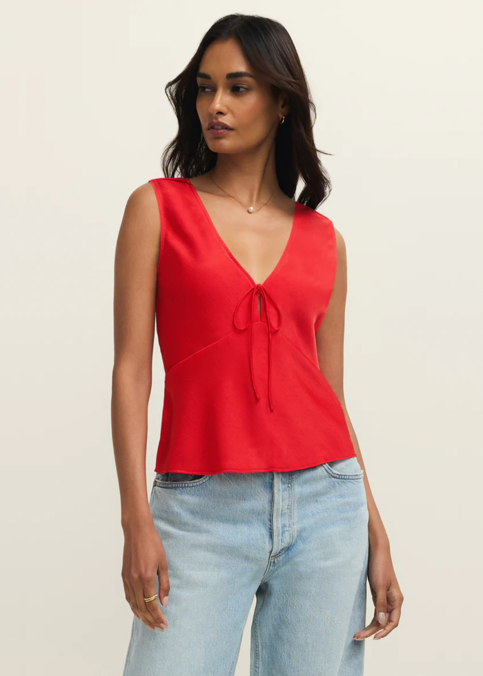 Woman wearing a red satin tank top with a front bow tie and jeans against a white background
